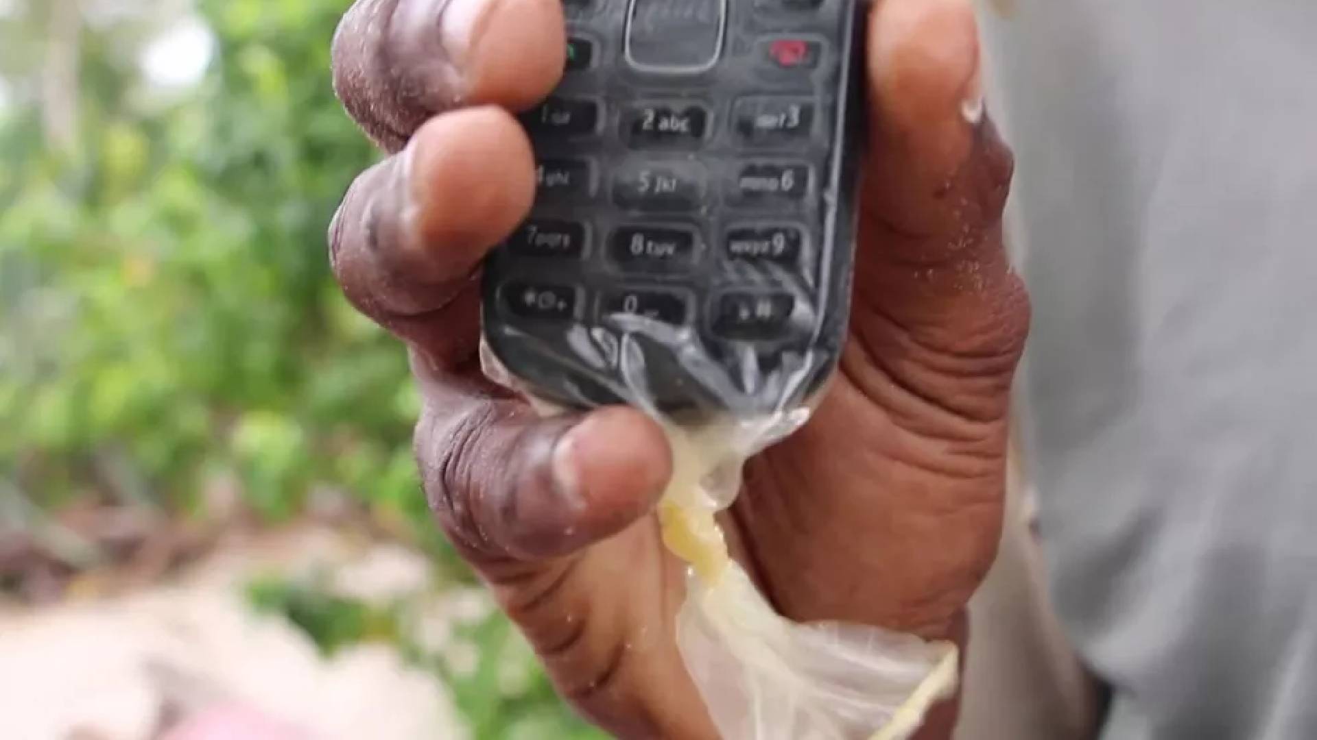 Pessoa segurando um celular com um preservativo. Utilidades da camisinha