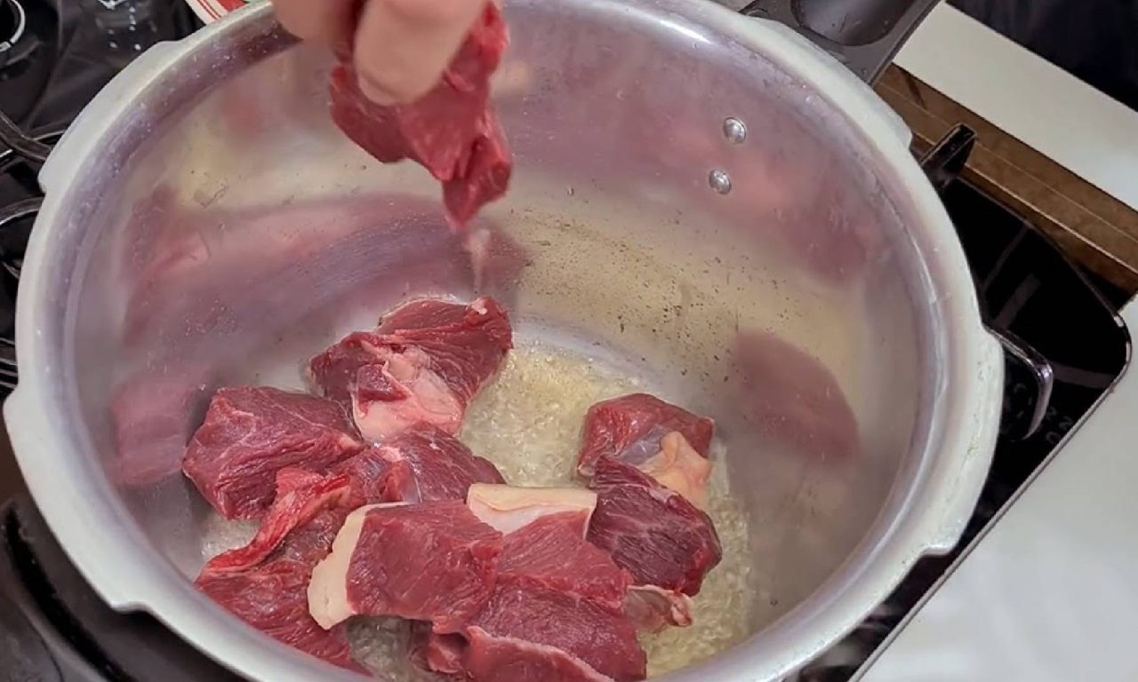 Pessoa colocando carne para fazer na panela de pressão