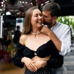 Homem fala no ouvido de uma mulher que sorri ao receber elogio