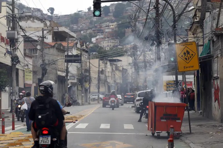 Durante operação policial contra o Comando Vermelho, bandidos ordenam fechamento de comércio e usam lixeiras incendiadas para bloquear a via no Rio de Janeiro.