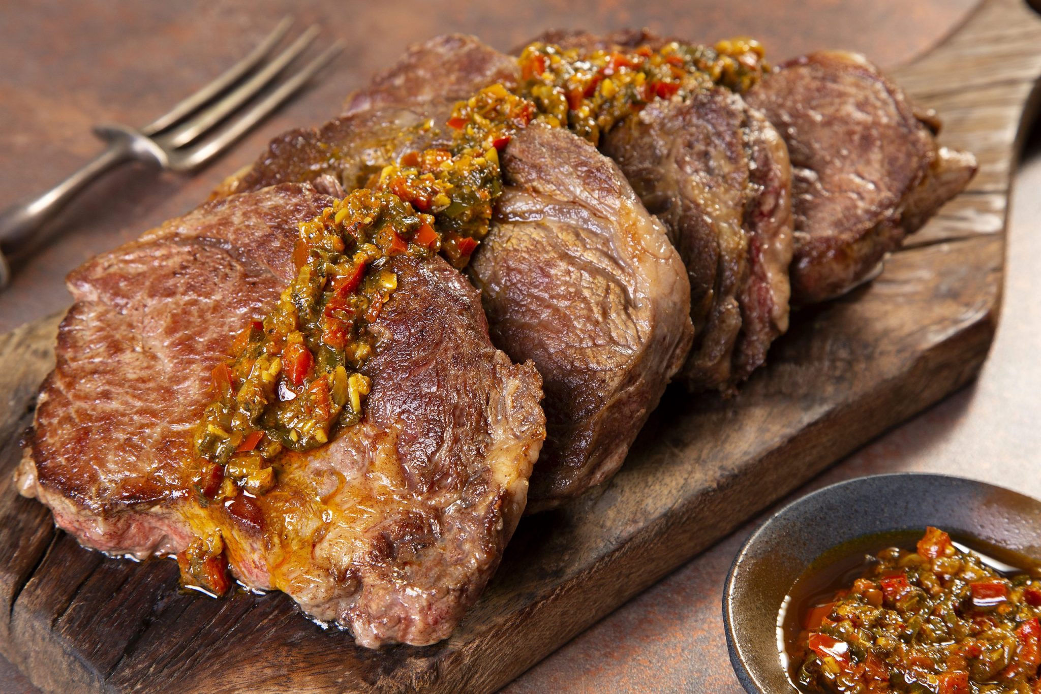 Pedaços de carne grelhada suculenta cobertos com molho chimichurri verde, servidos em uma tábua de madeira rústica