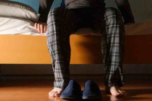Pessoa acordada durante a madrugada ao lado da cama, representando idas frequentes ao banheiro para urinar durante a noite