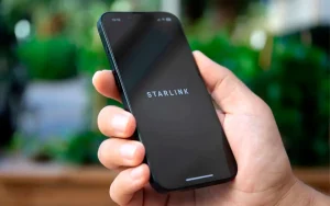 Pessoa segurando celular em área rural sem sinal, representando conexão direta entre satélites e smartphones