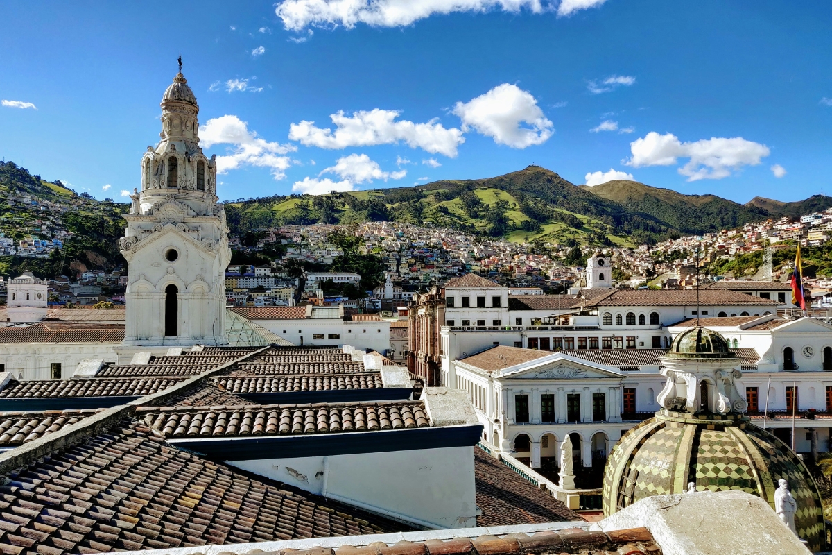 Pertinho do Brasil, um país ainda pouco explorado por turistas brasileiros reúne ilhas paradisíacas, centros históricos preservados e paisagens que parecem saídas de outro planeta. Em um território relativamente pequeno, o destino combina montanhas, vulcões, praias, biodiversidade e uma culinária cheia de personalidade. Esse país é o Equador, localizado na América do Sul e atravessado pela linha imaginária que divide os hemisférios Norte e Sul. Além disso, usa o dólar como moeda oficial, o que pode facilitar o planejamento financeiro de quem pretende viajar para fora do Brasil. A capital Quito é uma das grandes portas de entrada. Situada a quase 3 mil metros de altitude, a cidade é cercada por montanhas e vulcões, com passeios que oferecem vistas impressionantes da região andina. Um dos pontos mais procurados é o teleférico, que leva os visitantes a áreas elevadas e permite observar a cidade de cima. Já o Centro Histórico concentra igrejas, praças, construções coloniais e prédios oficiais, sendo reconhecido pela UNESCO como Patrimônio Mundial. Outro atrativo conhecido é a Mitad del Mundo, parque que marca a divisão entre os dois hemisférios. O espaço reúne monumento, museus, lojas e experiências voltadas à geografia e à cultura local. Além da capital, Cuenca também aparece entre os destinos mais charmosos. Fundada no século XVI, a cidade preserva ruas históricas, arquitetura colonial, museus e praças que ajudam a contar parte importante da história do país. Mas o grande cartão-postal está no Pacífico. As Ilhas Galápagos são famosas pela biodiversidade única e pela sensação de contato direto com uma natureza preservada. A viagem também passa pelo paladar. Pratos como bolón de verde, encebollado de pescado, locro de papas e preparos com caranguejo mostram que o destino surpreende não apenas pelas paisagens, mas também pela comida