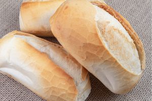 Comprar cinco ou dez pães franceses continua sendo possível, mas o valor não pode ser calculado apenas pelo número de unidades. A padaria deve pesar o produto e definir a cobrança com base no preço do quilo. A exigência está na Portaria nº 181/2021 do Instituto Nacional de Metrologia, Qualidade e Tecnologia (Inmetro). O texto determina que o pão francês, também conhecido como pão de sal, seja comercializado somente por peso, embora cada unidade possa ter qualquer massa. Por que a venda é feita por quilo A regra busca impedir que consumidores paguem o mesmo preço por pães de tamanhos diferentes. Ao discutir a norma que antecedeu a portaria atual, o Inmetro explicou que a pesagem reduziria erros encontrados na comercialização por unidade. Na prática, o cliente pode pedir a quantidade de pães que desejar. Antes da cobrança, porém, os produtos precisam passar pela balança, e o total deve corresponder ao peso efetivamente levado. O que a padaria precisa cumprir O preço do quilo deve ficar próximo ao balcão, em local de fácil visualização. A portaria também exige que os números tenham, no mínimo, cinco centímetros de altura. Já a balança precisa ter divisão igual ou inferior a cinco gramas e mostrar tanto o peso medido quanto o preço a pagar. Apesar de voltar a circular nas redes sociais, a obrigação não é recente. A venda por peso foi regulamentada em 2006 e consolidada pela portaria de 2021, atualmente indicada pelo Inmetro como referência para o setor.