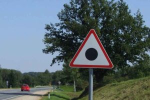 placa triangular branca com as bordas vermelhas e um ponto preto no meio