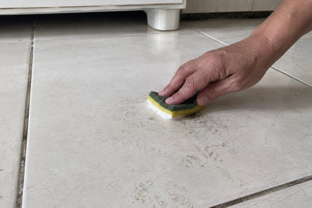 Pessoa aplica pasta de limpeza sobre marca impregnada em piso de porcelanato