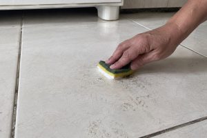 Pessoa aplica pasta de limpeza sobre marca impregnada em piso de porcelanato