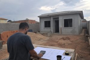 Casa em construção sobre lote residencial com planta e calculadora em primeiro plano