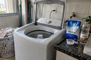 Máquina de lavar em lavanderia doméstica com sabão em pó e frasco de vinagre branco posicionados separadamente.