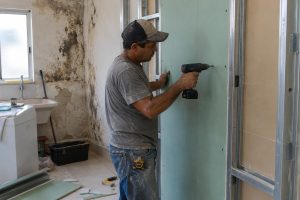 Pedreiro instala placa de gesso resistente à umidade diante de parede com pequenas manchas de mofo