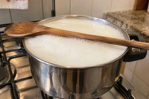 Colher de madeira atravessada sobre panela com leite formando espuma durante a fervura.