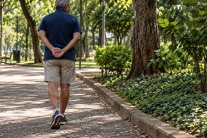 Pessoa caminha por uma praça com as mãos posicionadas atrás das costas
