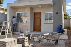 Casa térrea compacta em fase de construção com trabalhadores e materiais no terreno