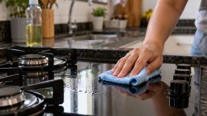Pessoa limpa o vidro preto de um cooktop com pano de microfibra e detergente neutro em uma cozinha residencial
