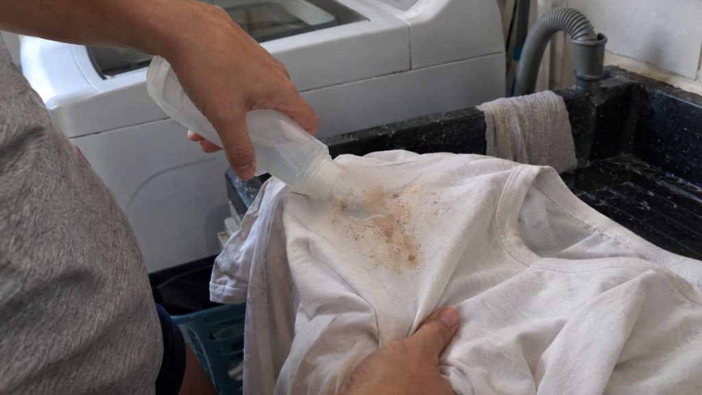 Pessoa aplica produto diretamente sobre uma mancha em camiseta antes da lavagem para evitar esfregar o tecido