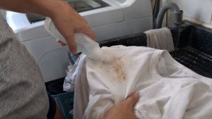 Pessoa aplica produto diretamente sobre uma mancha em camiseta antes da lavagem para evitar esfregar o tecido