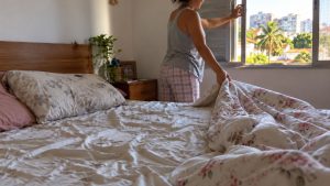 Pessoa deixa lençóis e cobertas expostos enquanto abre a janela do quarto antes de arrumar a cama