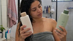 Mulher compara dois frascos de shampoo antes de lavar o cabelo em um banheiro residencial
