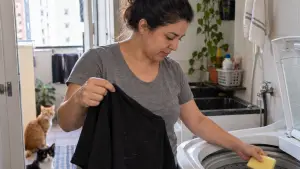 Mulher coloca esponja limpa na máquina de lavar junto a roupas pretas com pelos de gatos